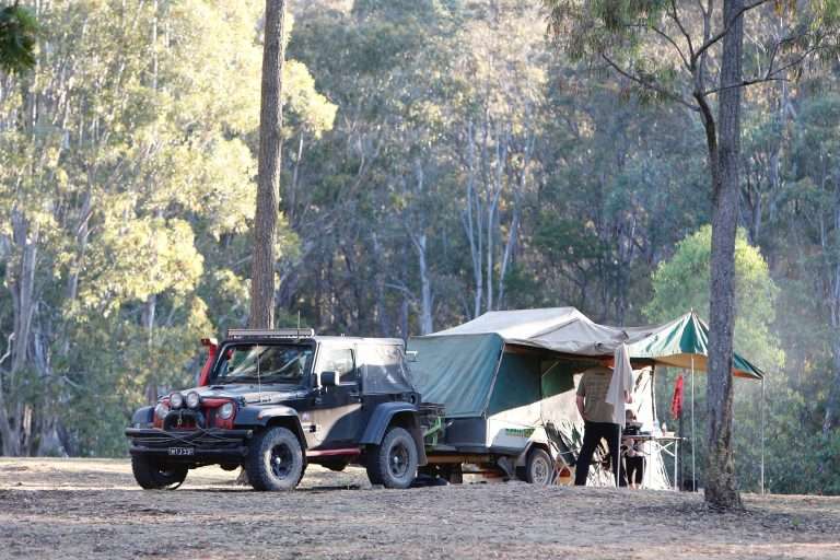 Jeep wrangler towing a camper behind it in the woods safely under its towing capacity